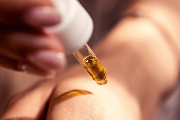 a hand holding a white oil dropper above skin